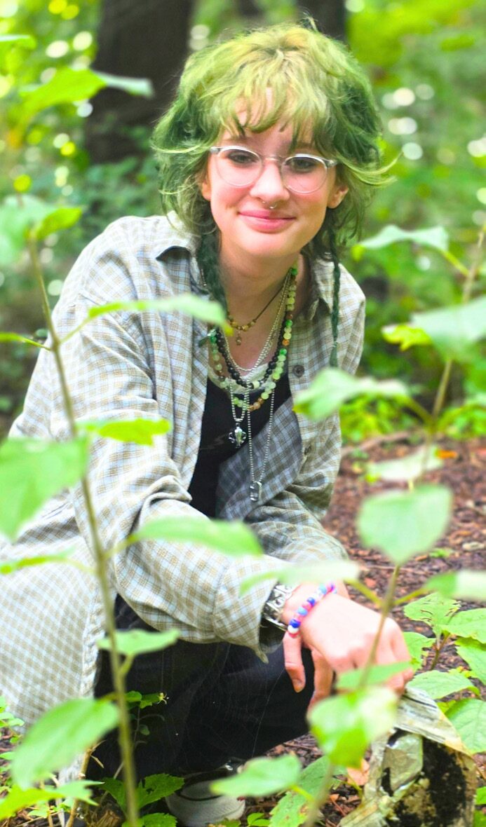 An Adolescent student kneels among green plants outdoors.